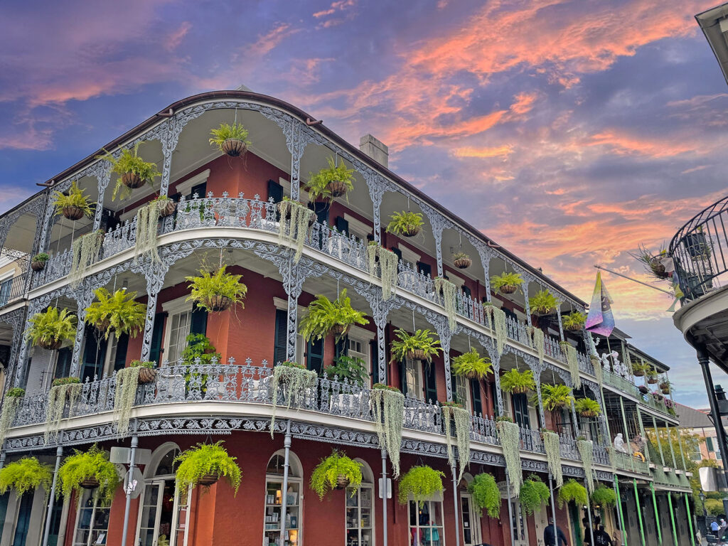 Historic corner building with ornate iron balconies and hanging ferns at sunset
